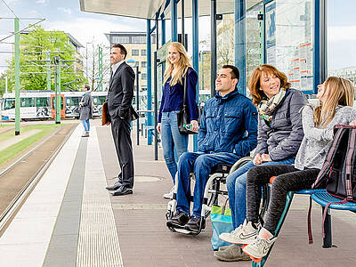 mehrere Menschen warten an einem Bahnsteig auf ihren Bus