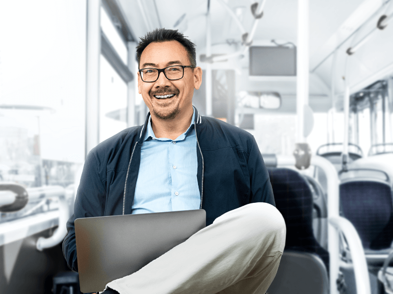 glücklicher Mann mit Laptop sitzt im Bus